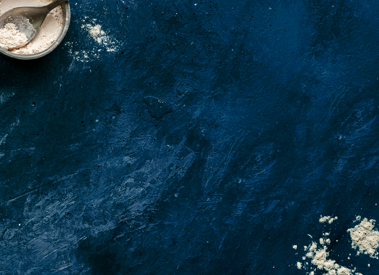 Illustration d’ambiance Ar Milin Coz, plan de travail bleu, farine étalée et bol de farine avec petite cuillère