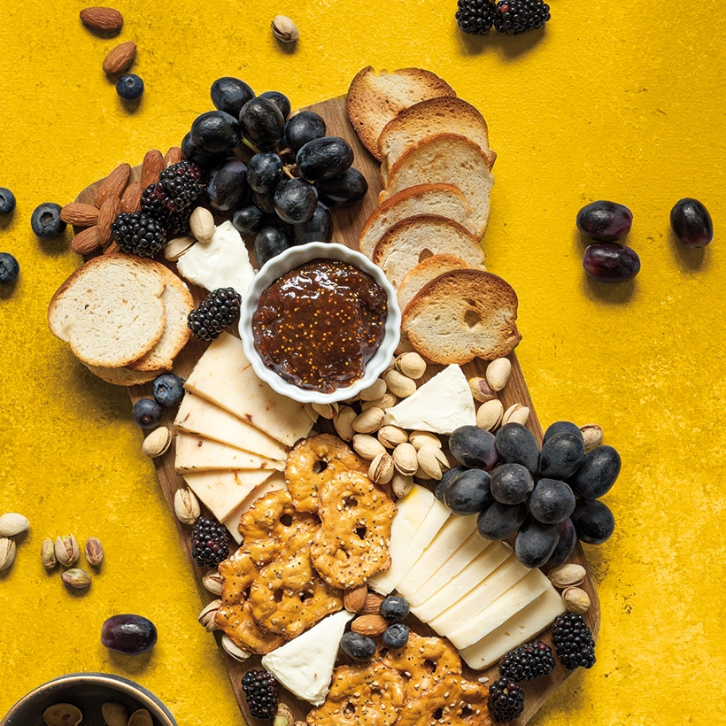 Image contexte M’Amour Guy Lesueur, planche apéritive, avec du chutney, des gâteaux, du fromage, du raisin, sur fond jaune, vue de dessus