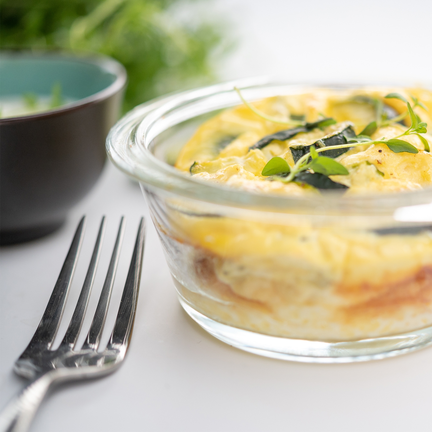 Photo culinaire flan de courgette, fourchette et grains de poivre au premier plan, salade et œuf à l’arrière plan, vue de face